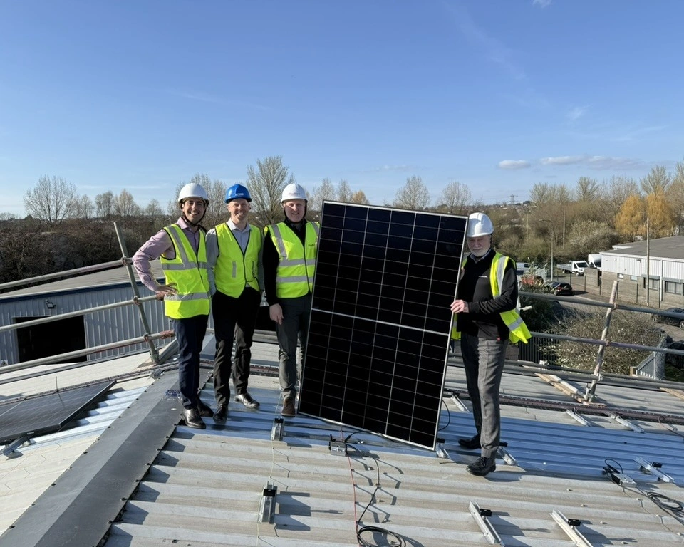 Four people in hi-vis vests and hard hats standing on the roof of Dudley's Aluminium in Cardiff, holding a solar panel during the installation