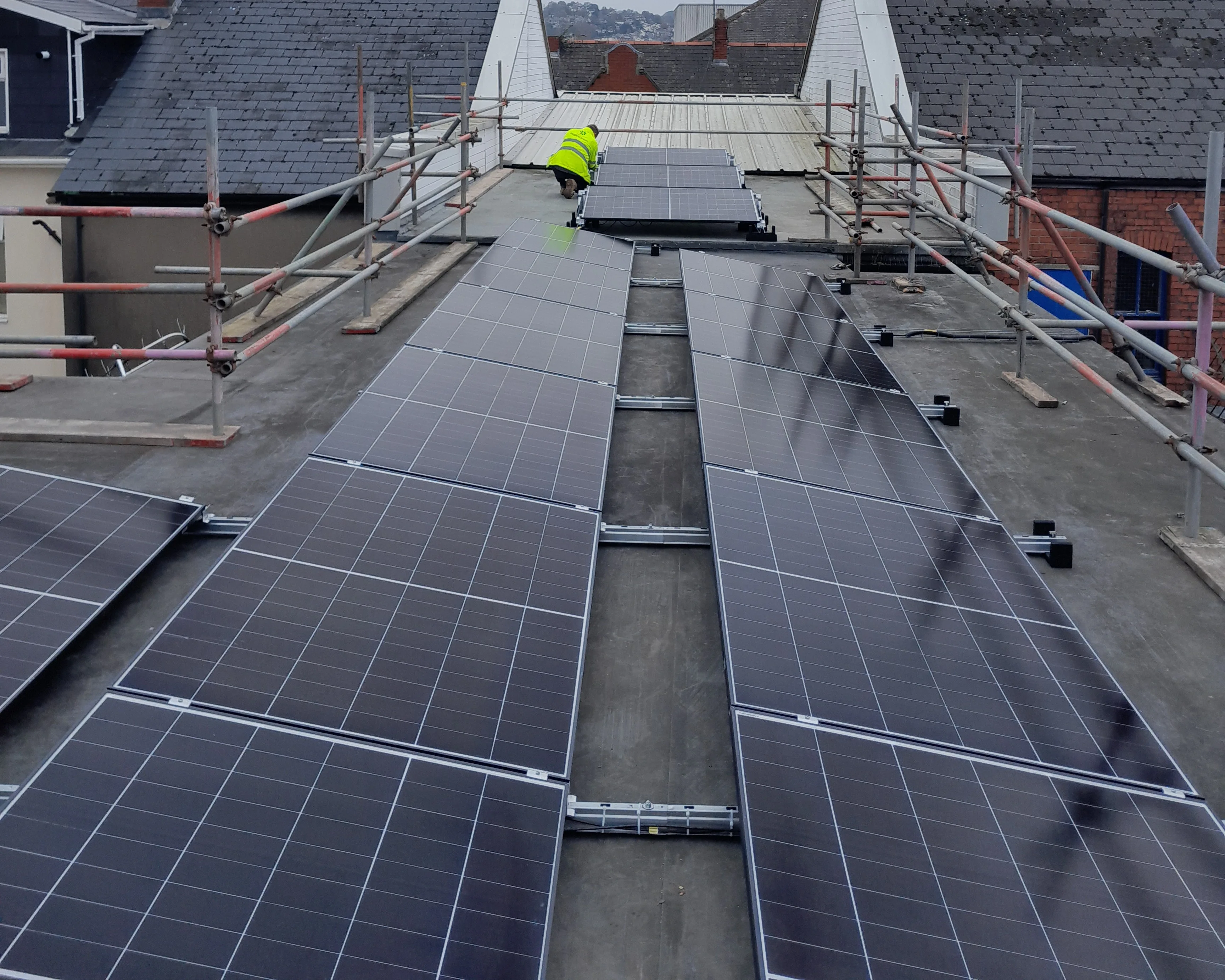 An installer fitting solar PV panels across the multiple roof orientations at iTec Skills' training centre in Newport, with scaffolding and edge protection in place