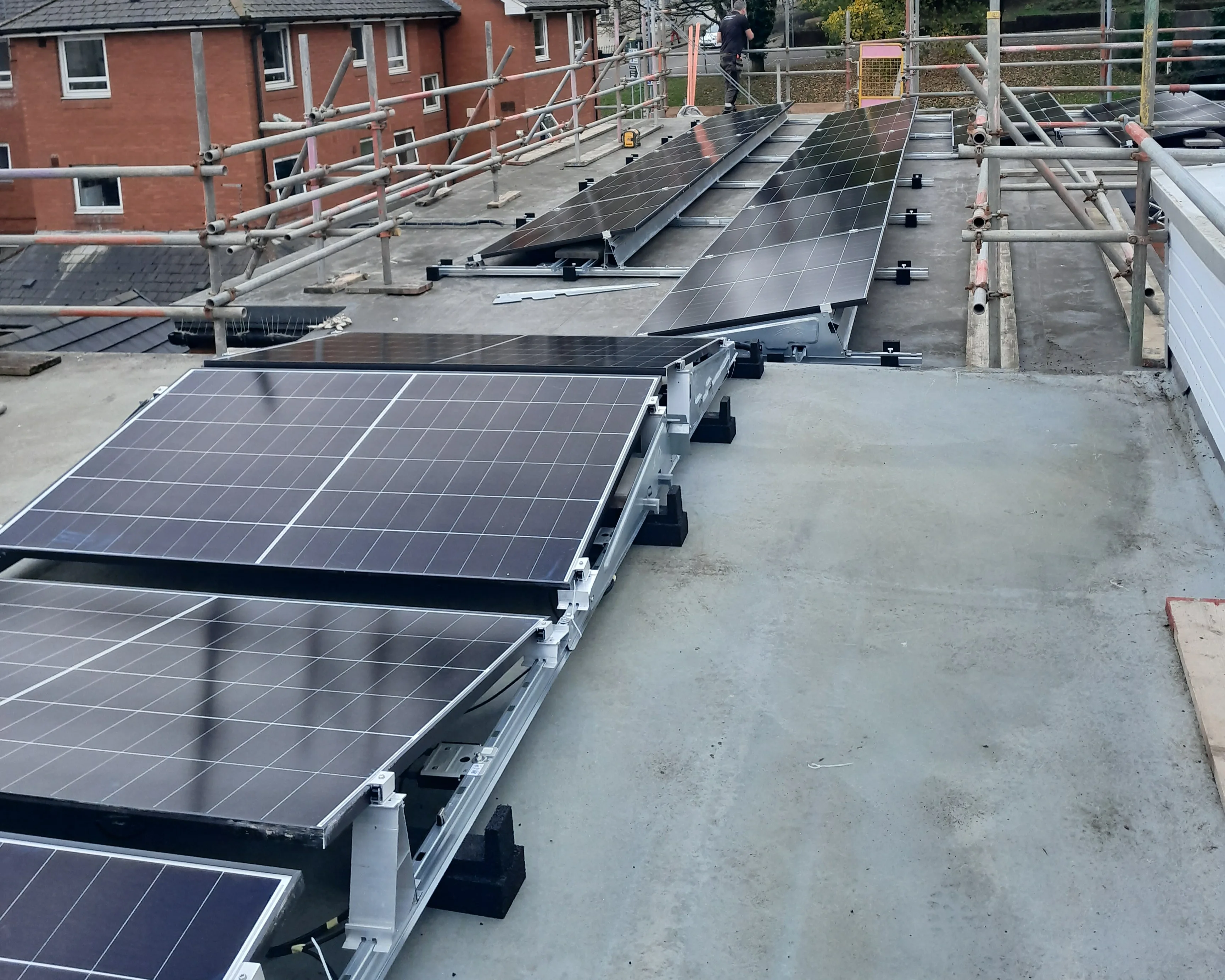 Solar PV panels mounted at different angles across the flat roof of iTec Skills' training centre in Newport, with an installer working on the array in the background