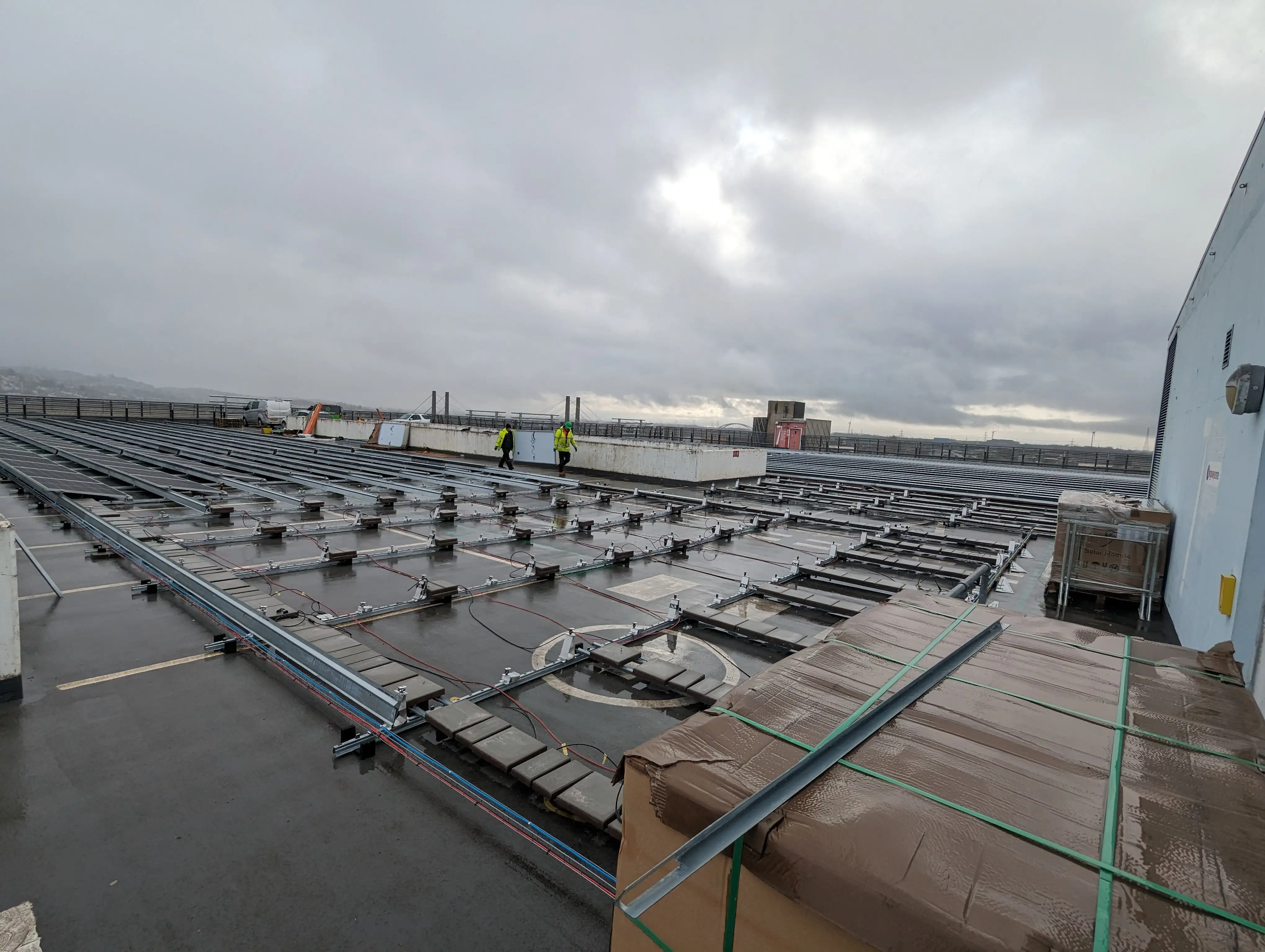 Engineers walking across the Kingsway Centre rooftop as solar panel mounting and DC cabling are installed