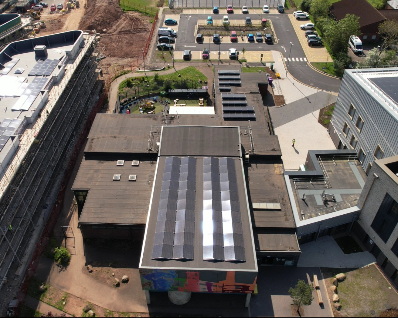 Aerial view of solar panels across the rooftops of Ringland Community Centre in Newport, with the building's mural and surrounding estate in view.