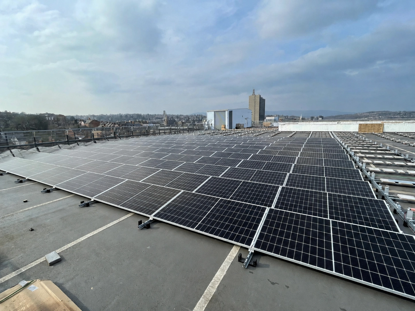 Rooftop solar panel array installed on a multi-storey car park, with a town skyline and hills visible in the background.