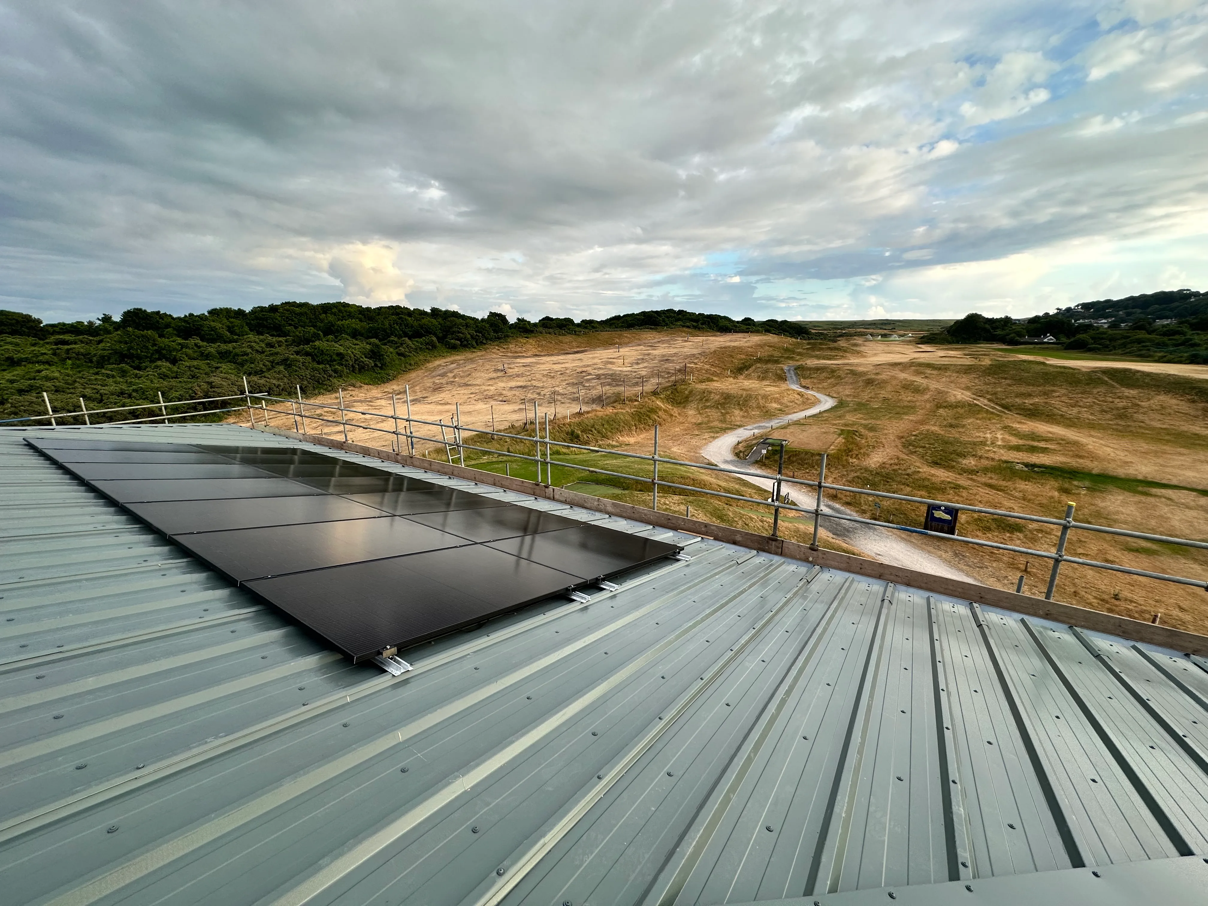 Rural rooftop solar PV installation, with panels mounted on a metal roof surrounded by open countryside.