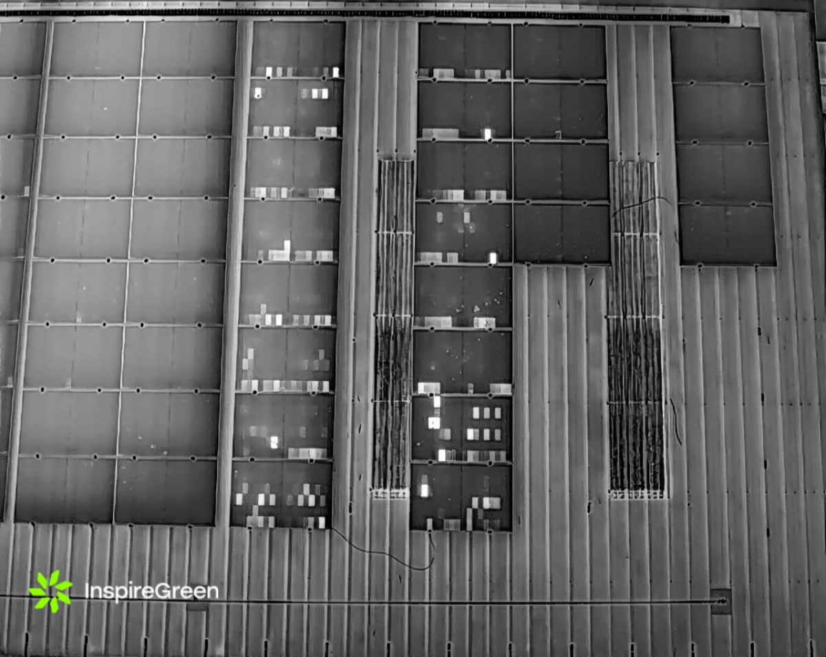 Aerial thermal image of a commercial rooftop solar array, with bright white patches showing individual cells running hotter than the panels around them.