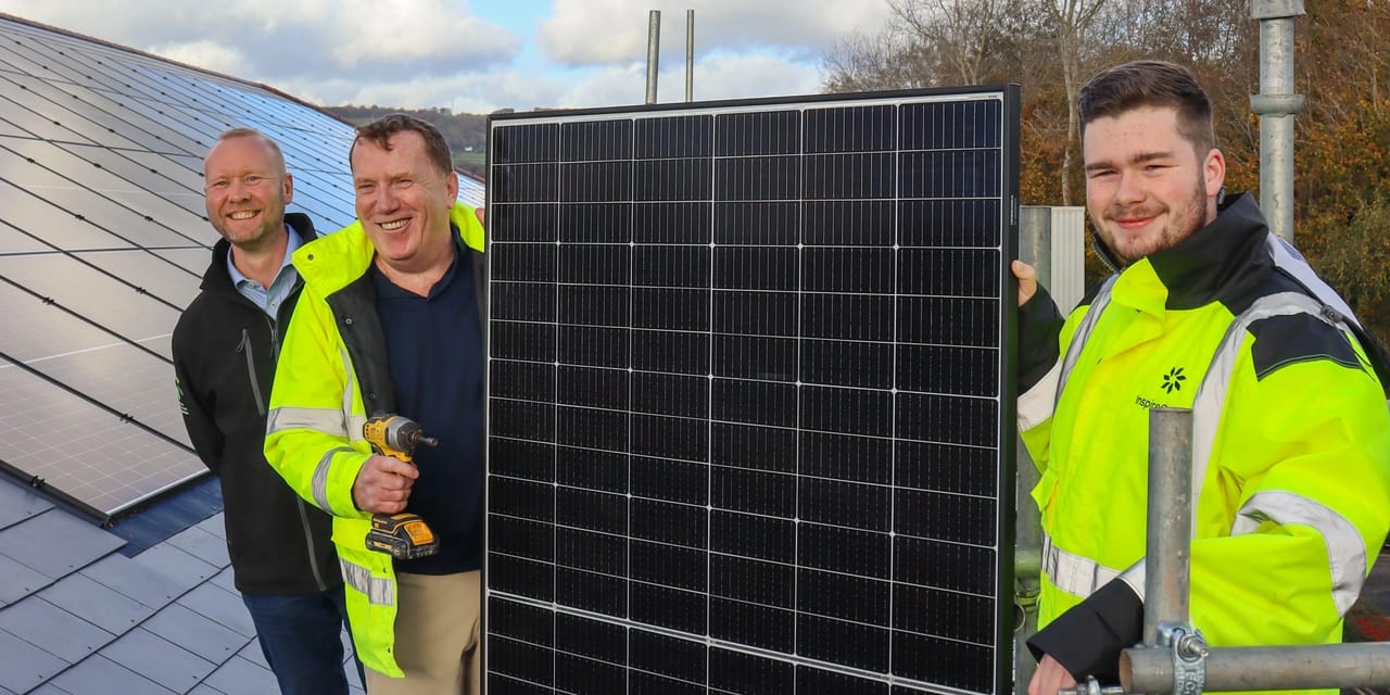 The InspireGreen team installing commercial solar panels on a rooftop, two in hi-vis jackets and one with a cordless drill beside a completed integrated roof array