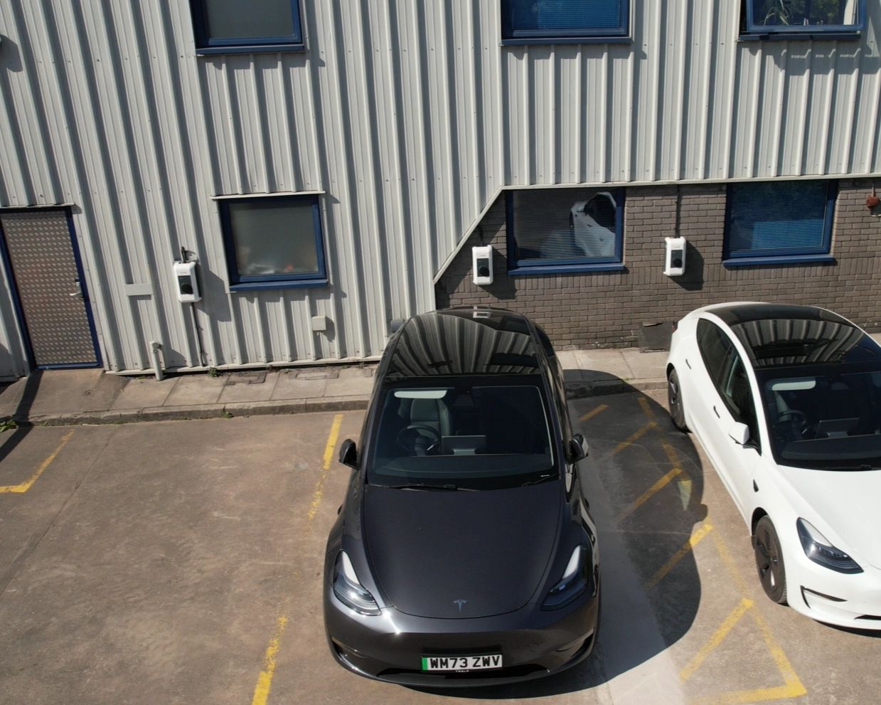 Two electric cars parked in marked bays at Dudley's Aluminium in Cardiff, with EV chargers mounted on the wall behind them