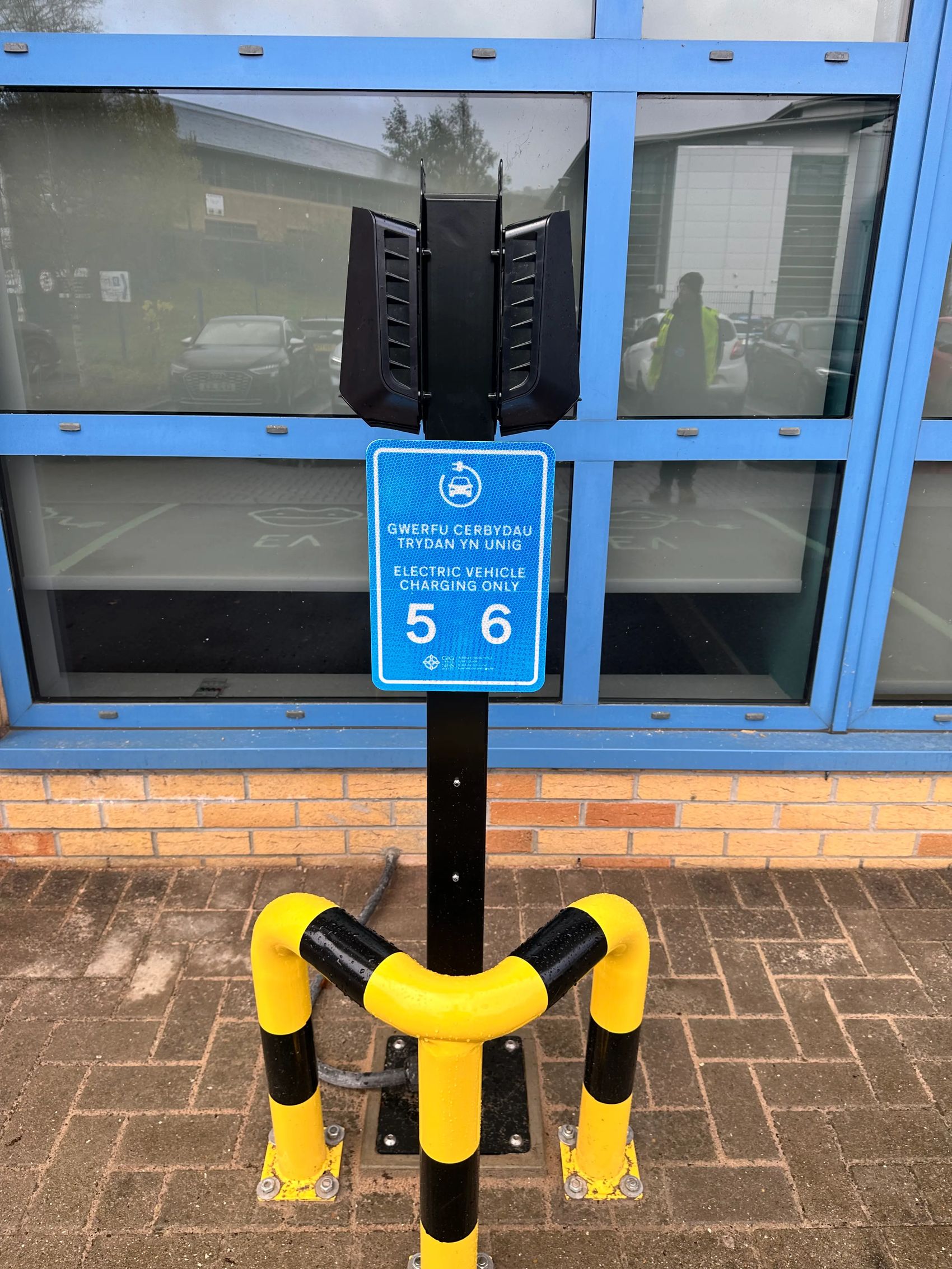Easee EV charger with custom bilingual signage and protective bollards at HEIW Nantgarw, installed by InspireGreen for workplace charging.