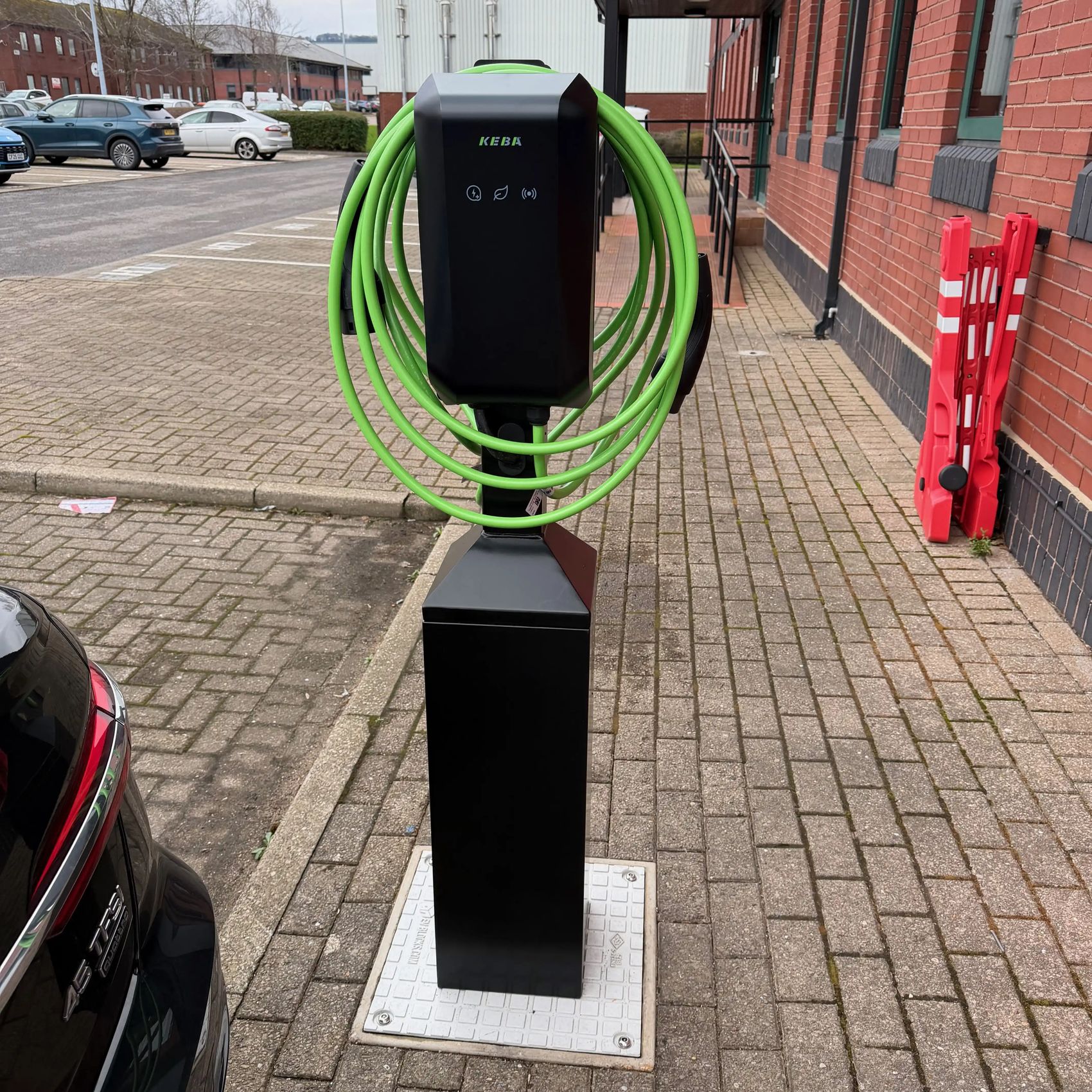 EV charging tower with two charge points and bright green cables in the car park at New Directions, Cardiff