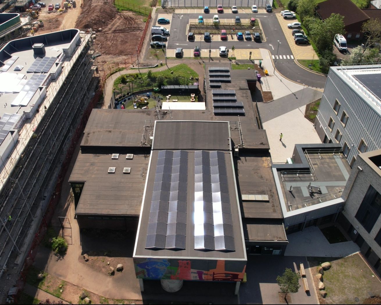 Aerial view of solar panels across the rooftops of Ringland Community Centre in Newport, with the building's mural and surrounding estate in view.