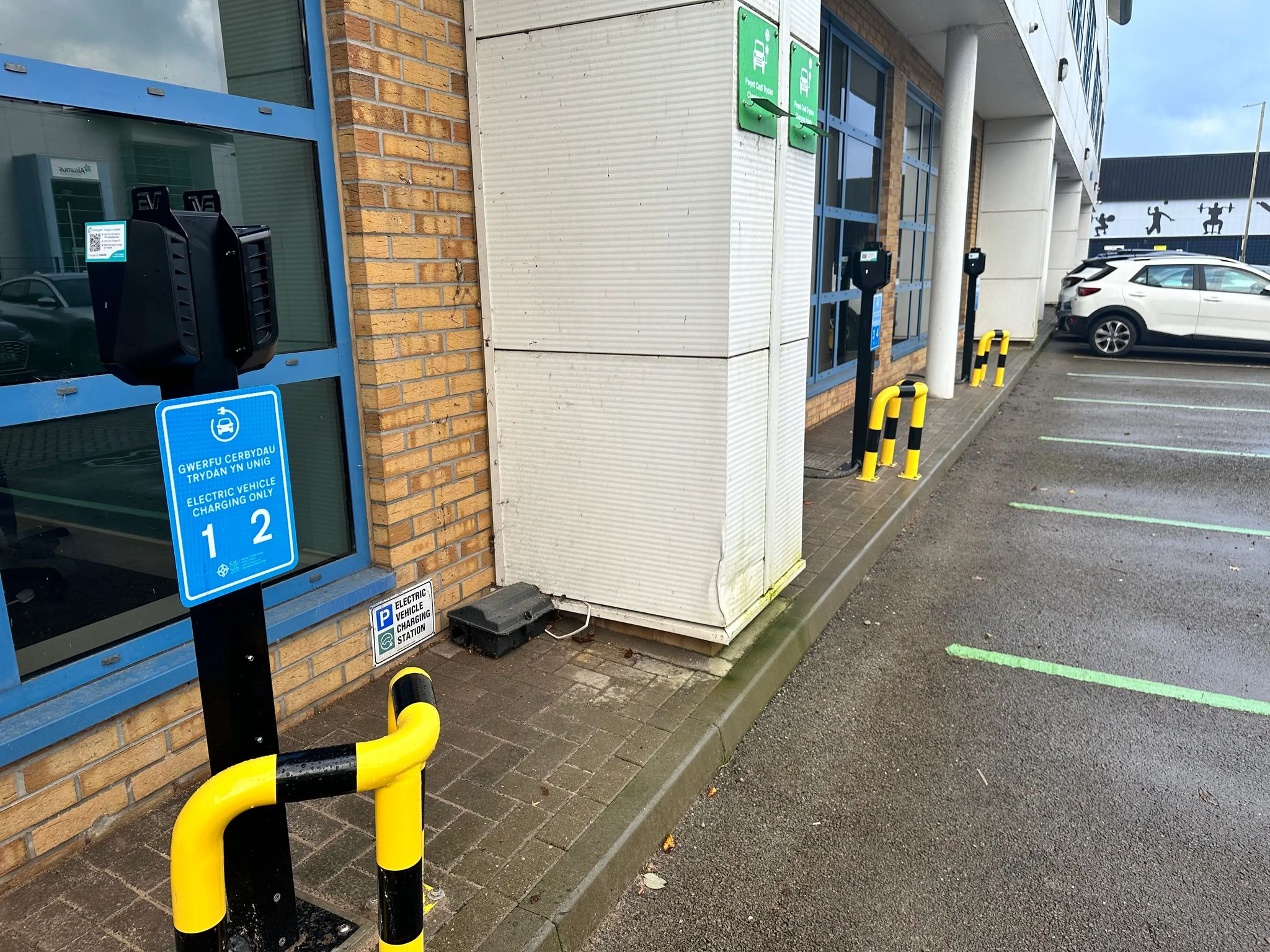 Workplace EV charging installation at HEIW Nantgarw by InspireGreen, showing pole-mounted Easee chargers, bilingual signage and protective bollards.