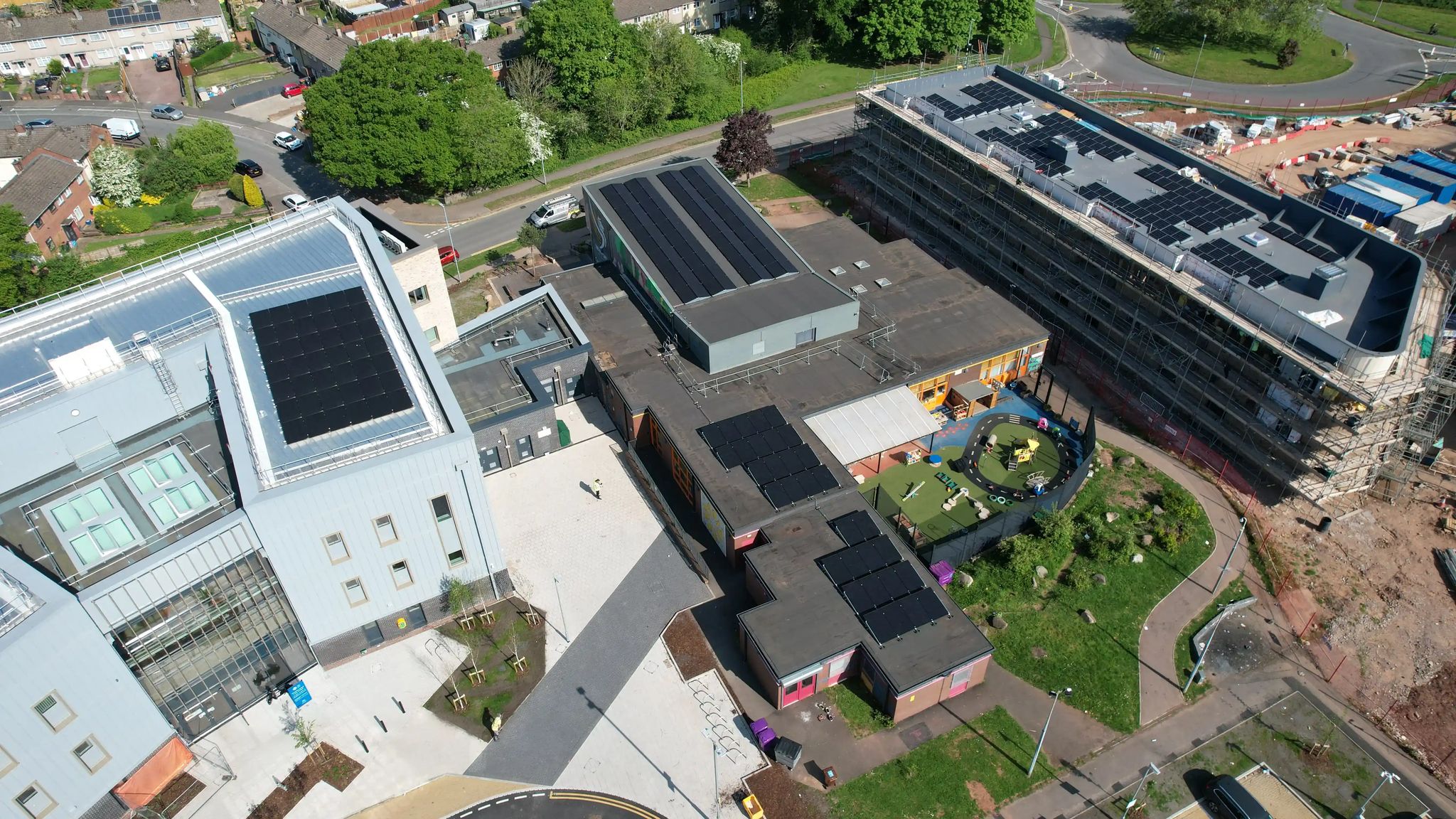 Drone shot of Ringland community centre in Newport, showing solar PV arrays on the flat and pitched roofs of multiple buildings, with a children's play area and surrounding housing.