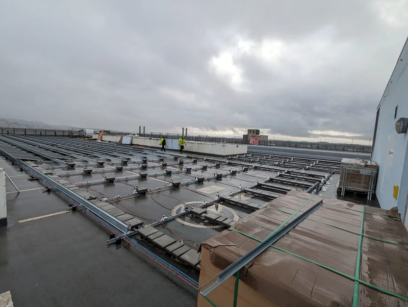 Engineers walking across the Kingsway Centre rooftop as solar panel mounting and DC cabling are installed